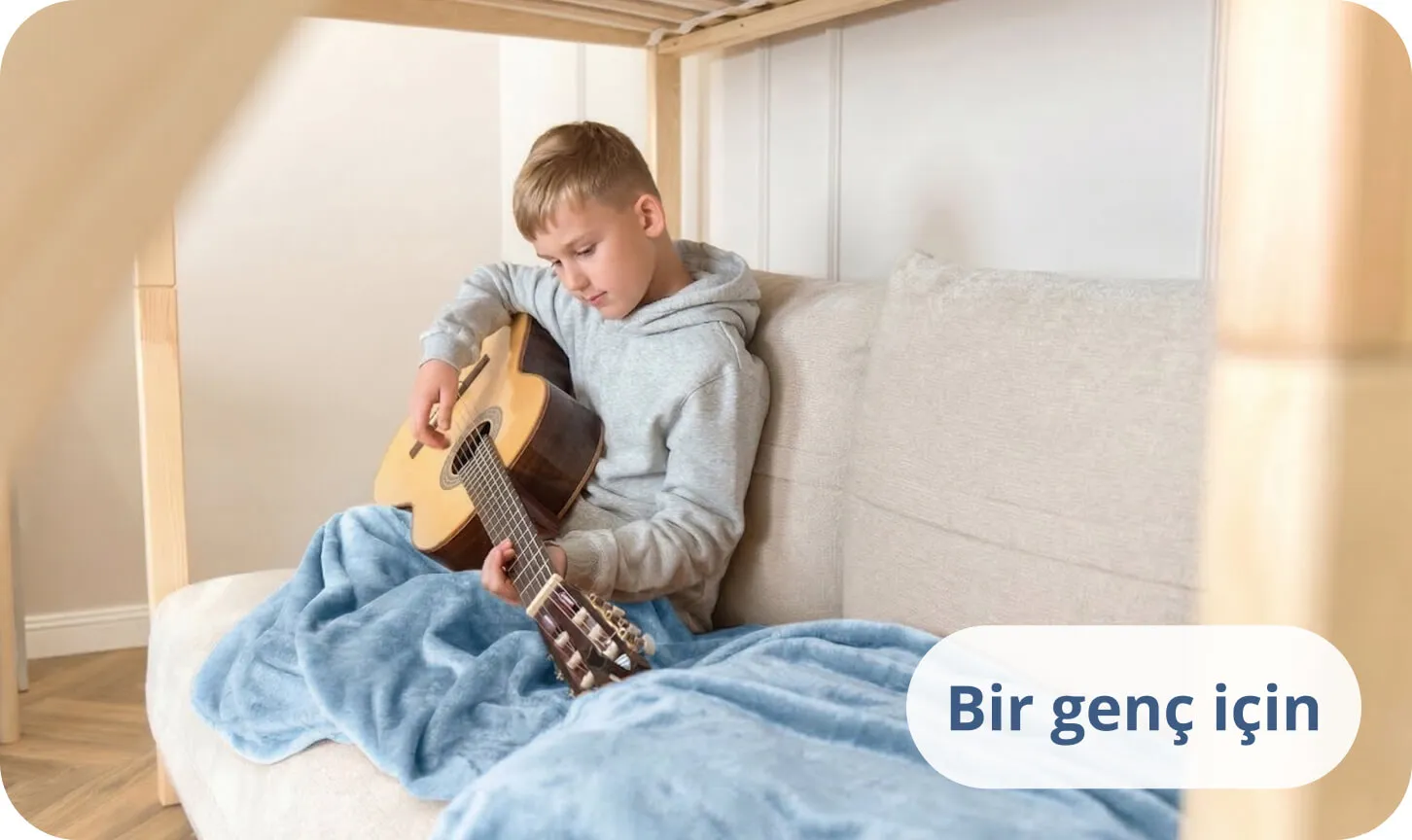 Mavi bir battaniyeye sarılmış, yatakta akustik gitar çalan genç.